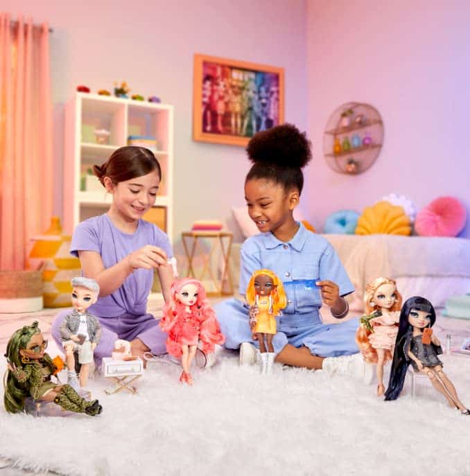 Two girls joyfully play with colorful dolls in a cozy, pastel-colored room.