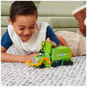 Joyful boy playing with a green toy truck on a cozy rug in a cheerful setting.