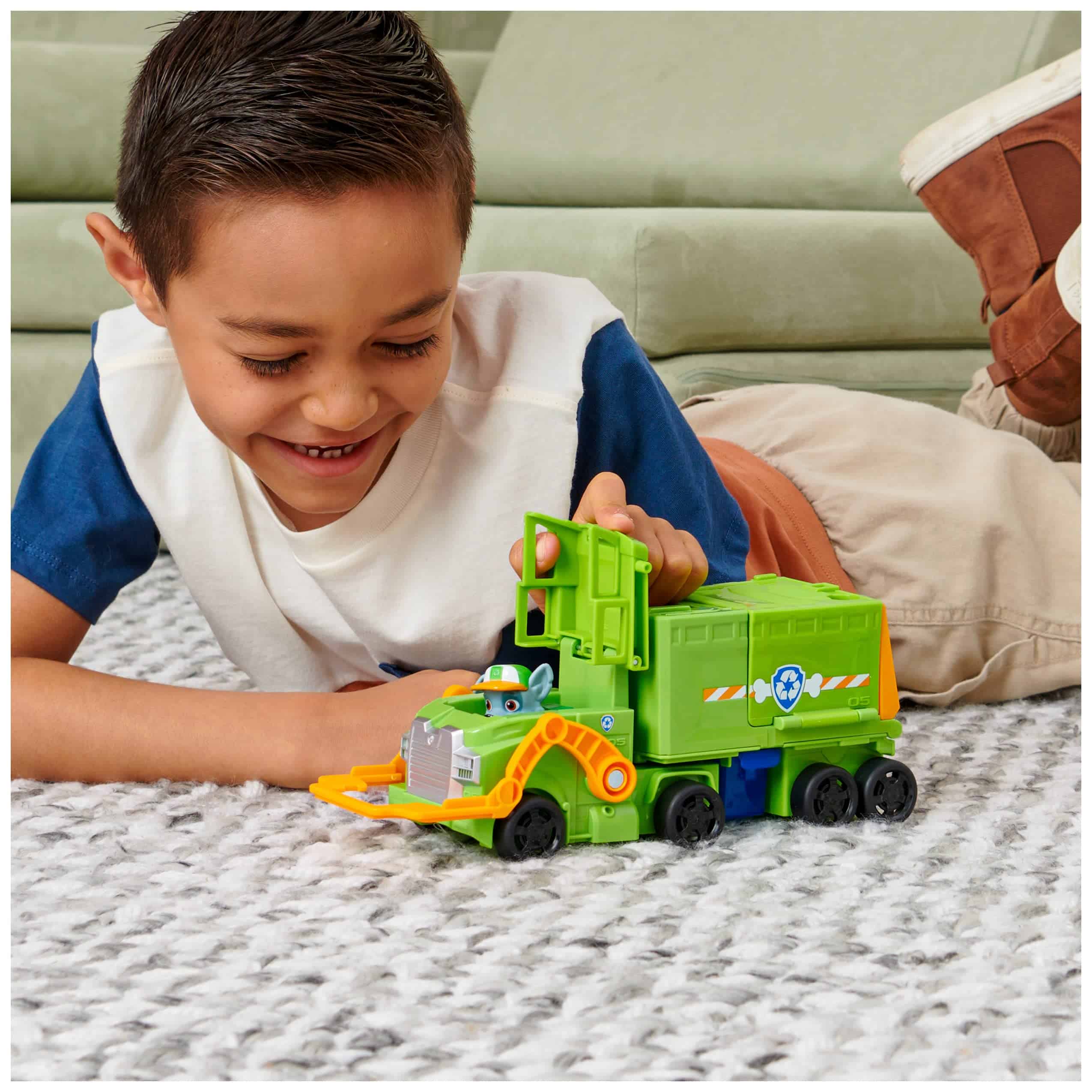 Joyful boy playing with a green toy truck on a cozy rug in a cheerful setting.