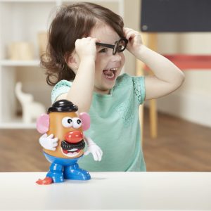 Joyful child wearing green shirt plays with colorful Mr. Potato Head in imaginative setting.