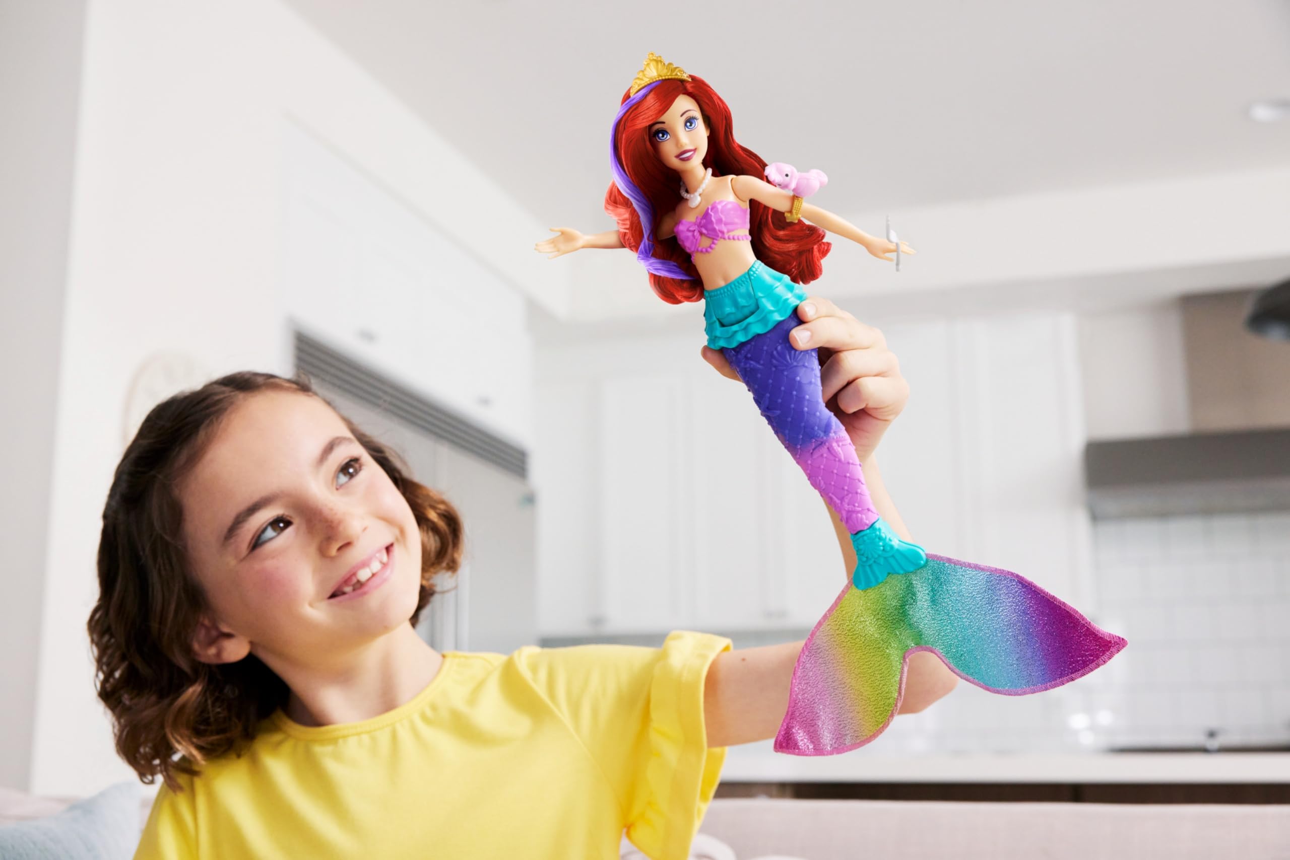 Young girl joyfully plays with a colorful mermaid doll in a bright living room.