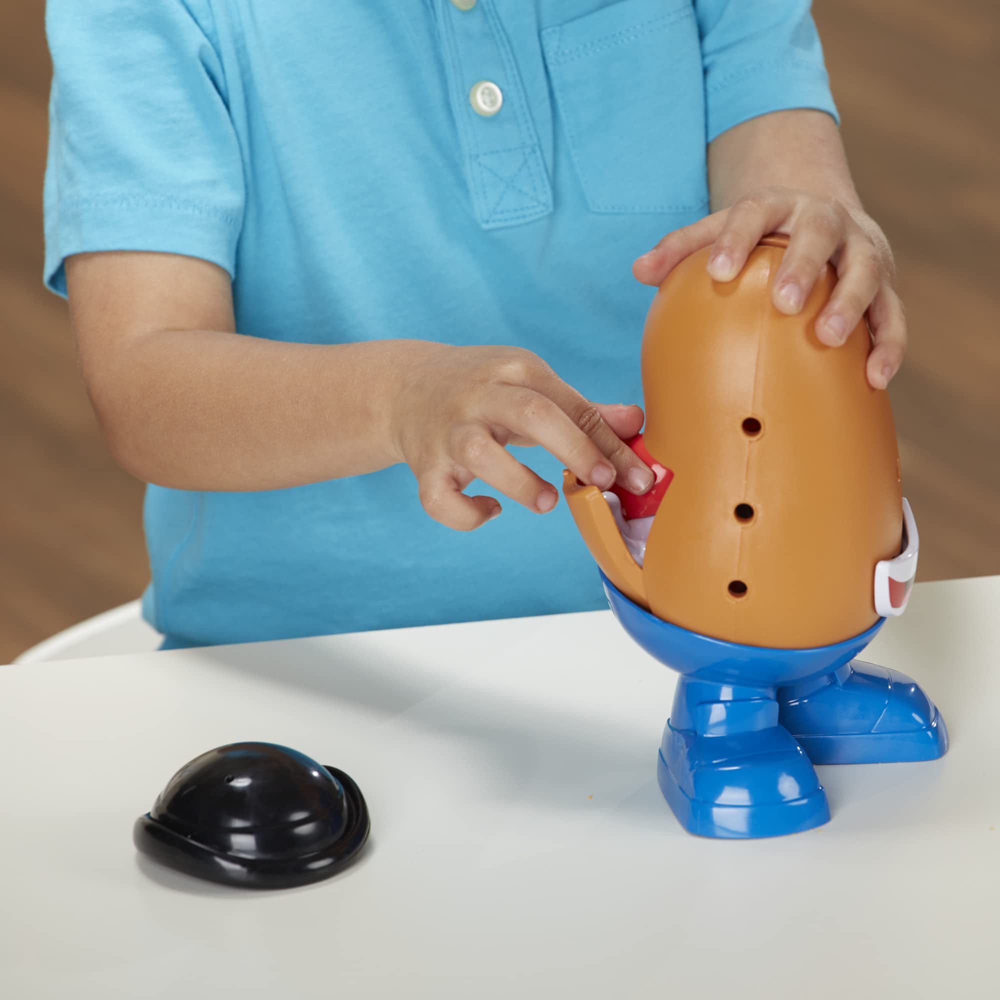 Child joyfully plays with Mr. Potato Head, inserting a red accessory in a vibrant setting.