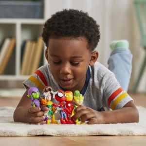 Young boy joyfully arranging colorful superhero action figures on a cozy rug.