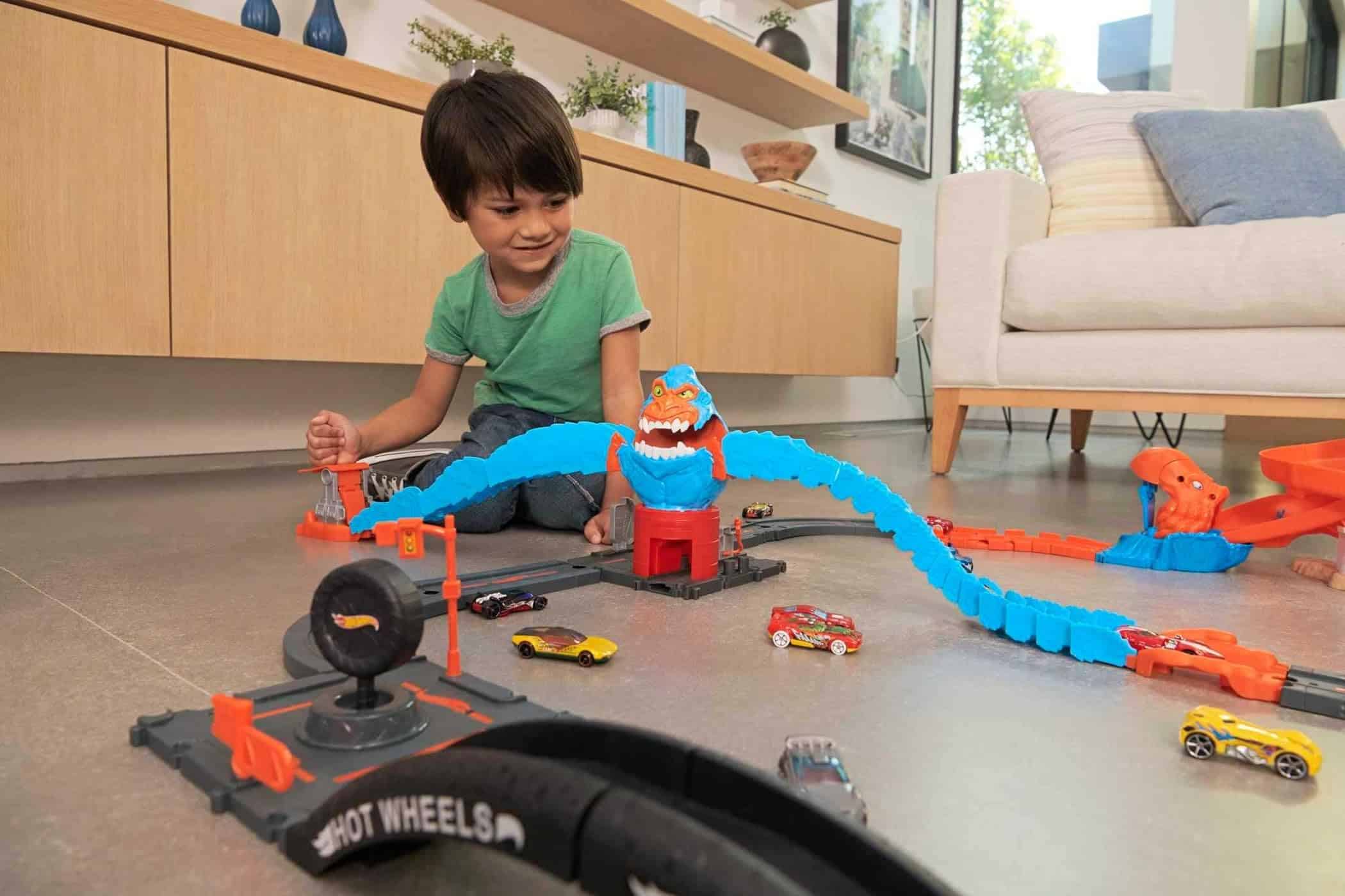 Young boy enjoys imaginative play with a vibrant toy racing track in a bright room.