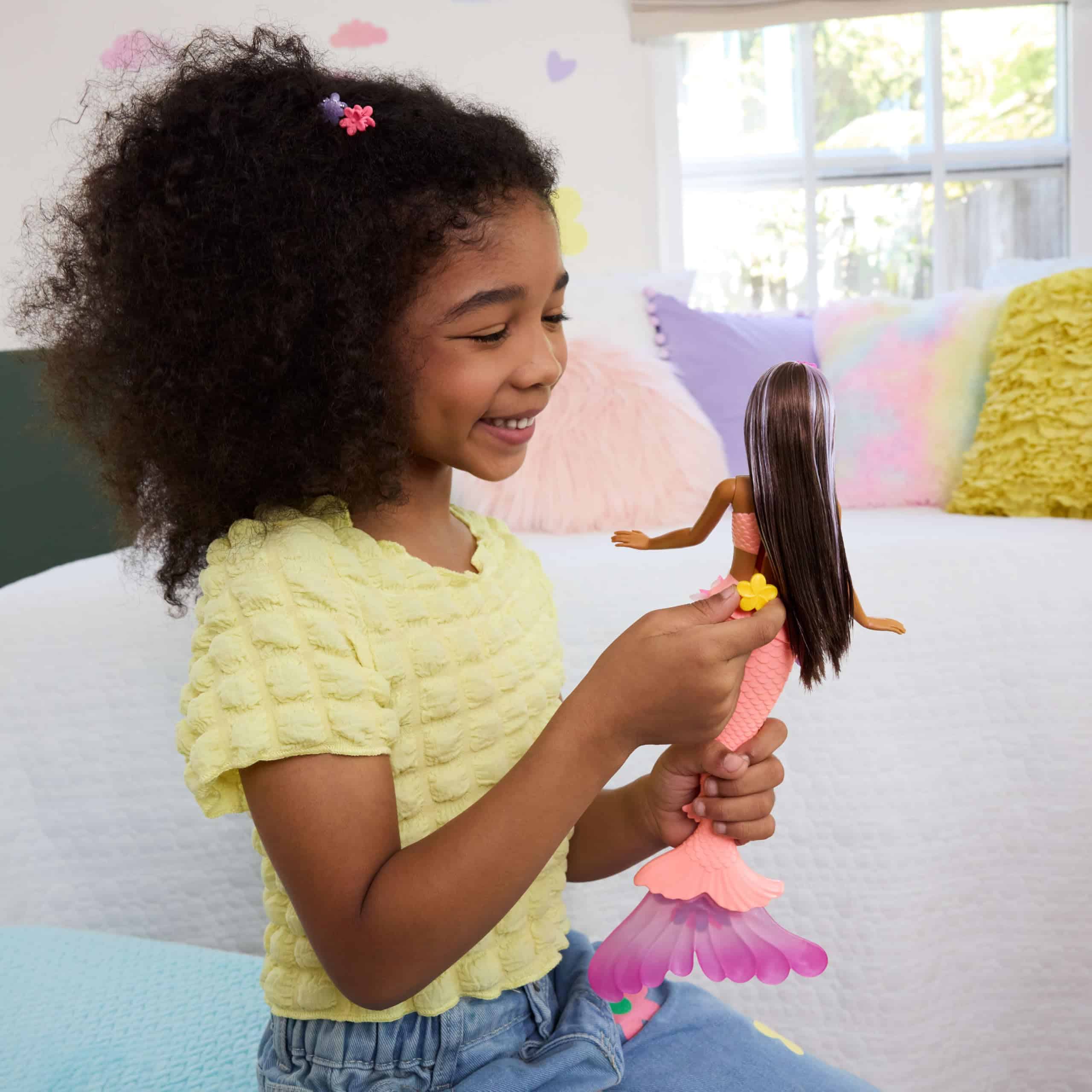 Young girl joyfully plays with a colorful mermaid doll in a bright, cheerful room.