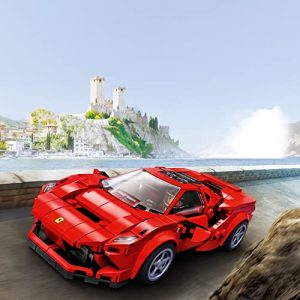 Red Ferrari F8 Tributo toy car on a coastal road with a castle backdrop.
