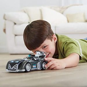 Boy plays with a glossy race car on a light wooden floor in a cozy living room.